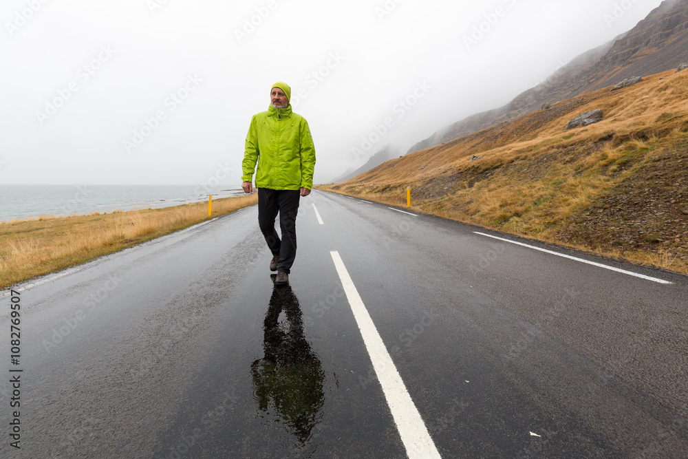 Fototapeta premium Ein Mann mit Regenjacke auf einer einsamen Straße in einer einsamen Gegend