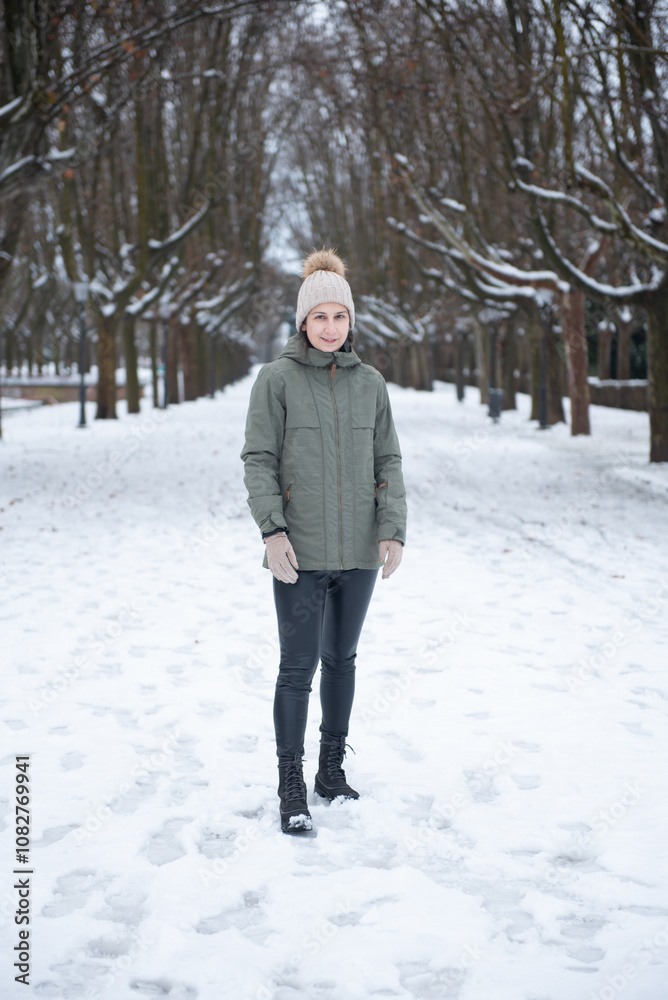 Mujer joven vestida con abrigo, gorro y botas, posando en parque nevado (con árboles de fondo) en Parque Grande, Zaragoza (España) Mujer joven vestida con abrigo, gorro y botas, posando en parque nevado (con árboles de fondo) en Parque Grande, Zaragoza (España)
