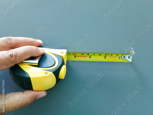 A hand held a black and yellow retractable tape measure. Measuring length, width and height concept, accuracy and precision.