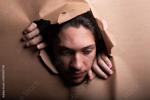 Man looking through a paper hole with his hands pushing the paper aside.