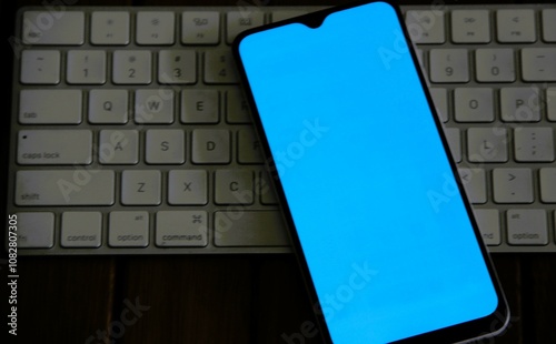 Celular fundo liso azul claro em cima de teclado - Cell phone with a plain black background on top of the keyboard photo