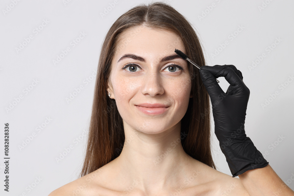 Beautician brushing client's eyebrows after henna dyeing procedure on light background, closeup Beautician brushing client's eyebrows after henna dyeing procedure on light background, closeup