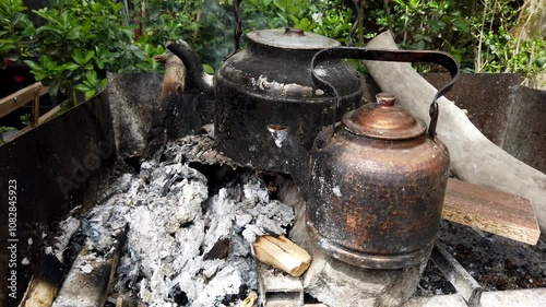 Two kettles rest on a wood fire, releasing white smoke from their spouts as they heat water for tea