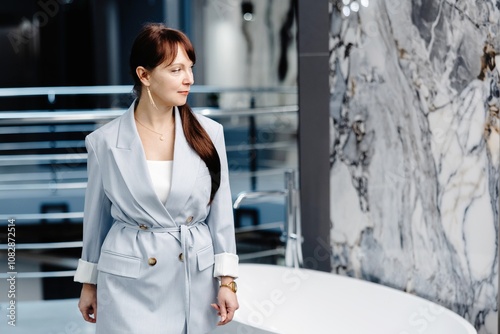 Woman in light suit stands near a freestanding bathtub in a modern showroom