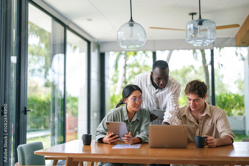 Two men and a woman, displaying diversity, are intently collaborating at a sleek office table, using a laptop and digital tablet, dressed in smart casual work attire. Two men and a woman, displaying diversity, are intently collaborating at a sleek office table, using a laptop and digital tablet, dressed in smart casual work attire.