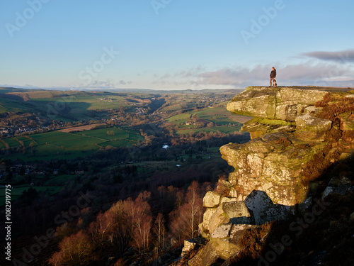 A person with a dog standing on a high rocky ledge, Curbar Edge in the Peak District, UK photo