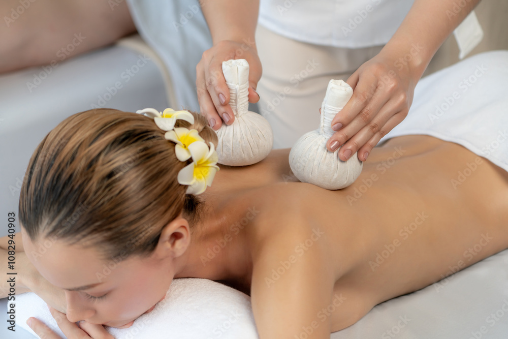 Hot herbal ball spa massage body treatment, masseur gently compresses herb bag on couple customer body. Tranquil and serenity of aromatherapy recreation in day lighting ambient at spa salon. Quiescent Hot herbal ball spa massage body treatment, masseur gently compresses herb bag on couple customer body. Tranquil and serenity of aromatherapy recreation in day lighting ambient at spa salon. Quiescent