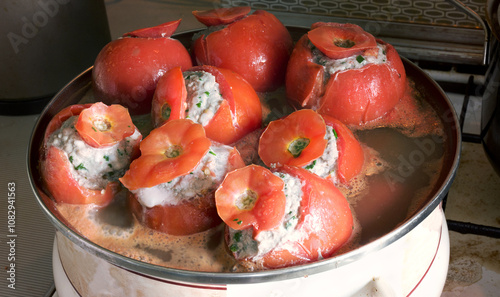 stuffed tomato cooking. Big enameled pot on a stove, full of tightly stuffed with minced meat with rice and herbs, tomatoes with caps of their cut top slices photo