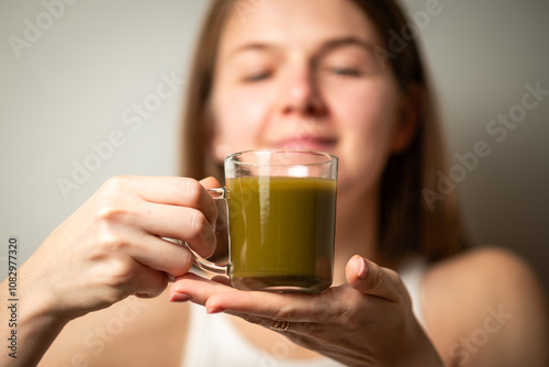 Kratom consumption concept:  female holds a ready to drink glass of green liquid, powdered kratom melted in hot water, kratom tea, close up photo, selective focus