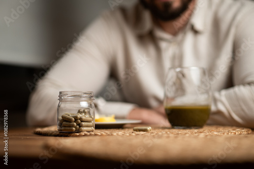 Kratom consumption concept: male bearded hipster holds a ready to drink glass of green liquid, powdered kratom melted in hot water, kratom tea, close up photo, selective focus