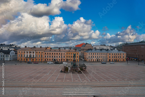 Senate Square in Helsinki, Finland, features the Alexander II statue, surrounded by neoclassical buildings like the Government Palace under dramatic clouds. photo