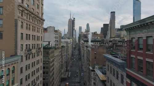 Camera pans over a busy street in New York City. Steam is rising from sewers and yellow cabs are driving down the street