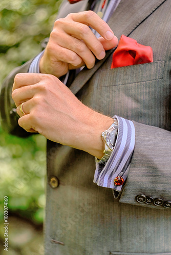 Fashionable man wearing a watch adjusting red handkerchief / pocket square in grey suit jacket.