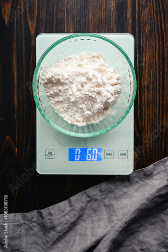 Weighing All-Purpose Flour on a Digital Kitchen Scale: Overhead view of bleached wheat flour in a glass bowl weighed on a food scale