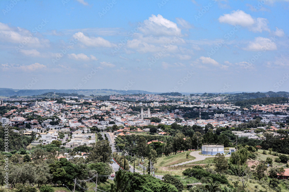 Obraz premium Scenic view of Vinhedo, São Paulo, showcasing urban and green landscapes with rolling hills and scattered buildings. Clear sky enhances the natural beauty of this Brazilian city.