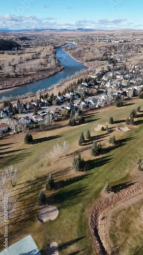 Aerial Vertical tracking shot over golf courses and waterfront home development with Canadian Rockies at background.
