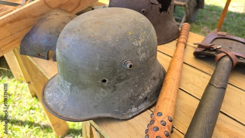 Vintage German Stahlhelm helmet from World War I or II on a wooden surface, accompanied by a spiked trench club and a field shovel with leather straps, evoking a wartime setting. photo