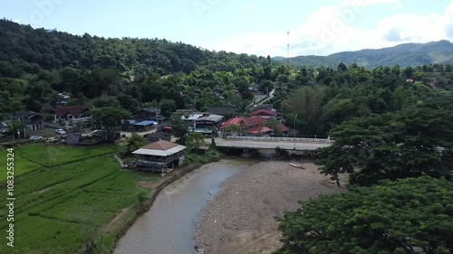 Road with bridge in village filled with trees and mountains in northern of Thailand