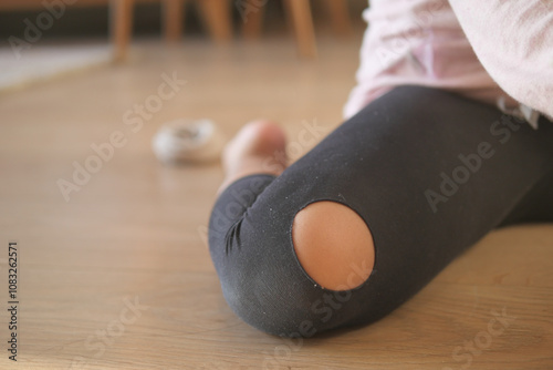 Close-Up of Worn-Out Leggings with Ripped Knee on Wooden Floor photo