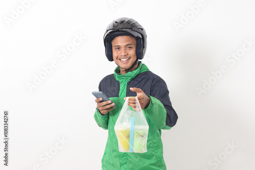 Portrait of Asian online taxi driver wearing green jacket and helmet delivering the beverages in plastic cup to customer, while using mobile phone. Isolated image on white background photo