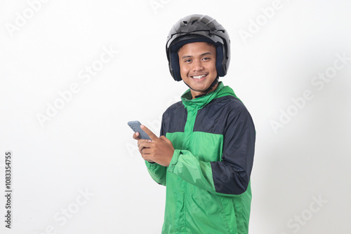 Portrait of Asian online taxi driver wearing green jacket and helmet holding mobile phone with smiling expression face. Isolated image on white background photo