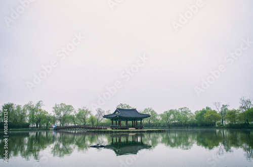 A serene dawn scene with a Korean traditional pavilion and trees reflected on the lake, surrounded by a gentle mist.v photo