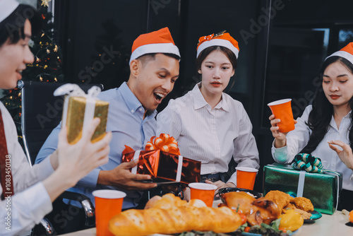 full length view of a group of business team wearing red Santa hat and exchange gift box together in the office for Christmas.