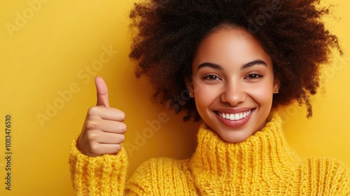 Close-up of a young woman in a yellow sweater giving a thumbs up while smiling, radiating positivity. The vibrant yellow sweater adds to the cheerful expression in this delightful image. photo