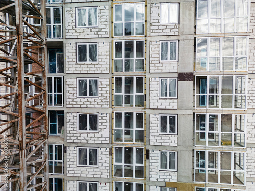 Modern apartment building under construction with large windows and scaffolding in a bustling city during the late afternoon light photo