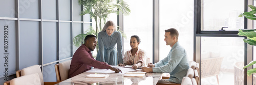 Diverse young business team working on project strategy together, meting for marketing analysis, reviewing paper reports on meeting table, pointing hands at documents, talking. Banner shot photo