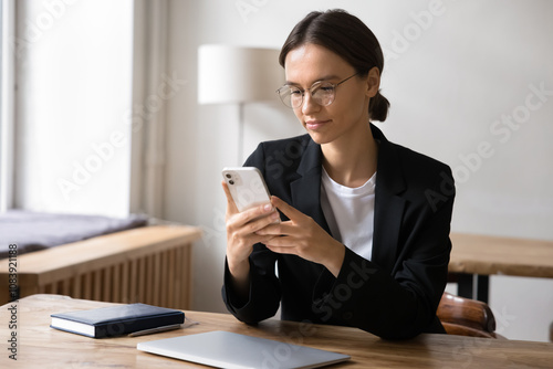 Attractive businesslady sit at workplace desk with smartphone, using mobile banking or financial management tools, planning, organizing workday, solve work-related matters efficiently via application photo