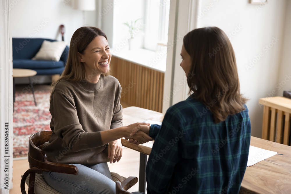 Fototapeta premium Two young attractive businesswomen, colleagues, client and manager finish meeting in office, shaking hands express respect. Closing commercial deal, confirm agreement, finalize business negotiations
