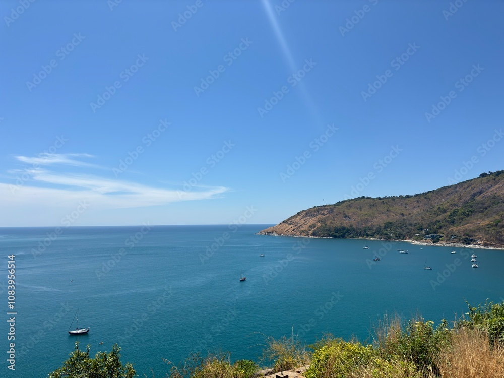 Obraz premium Breathtaking coastal view of a tranquil bay with boats near a hilly shoreline under a clear blue sky