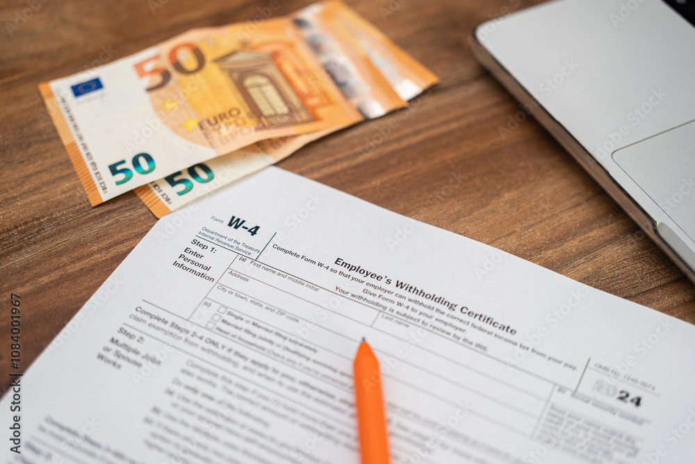 Obraz premium Employee filling out IRS form W-4 with euros and a laptop on a wooden desk. Payroll, tax withholding, and personal finance management concept 