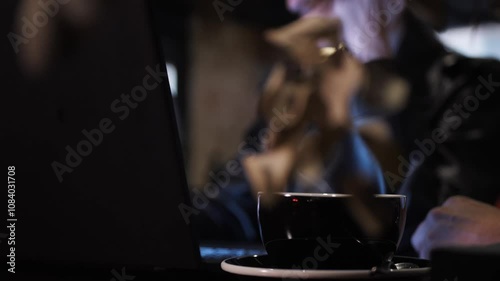 Cup of coffee on background of young woman typing on laptop keyboard. Three multiracial people working together on a project sitting at bar restaurant table. 