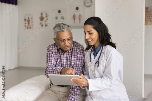 Older male patient asking about x-ray or diagnostic results on digital tablet during medical consultation in private clinic office. Young cardiologist explains diagnose or treatment plan to aged man