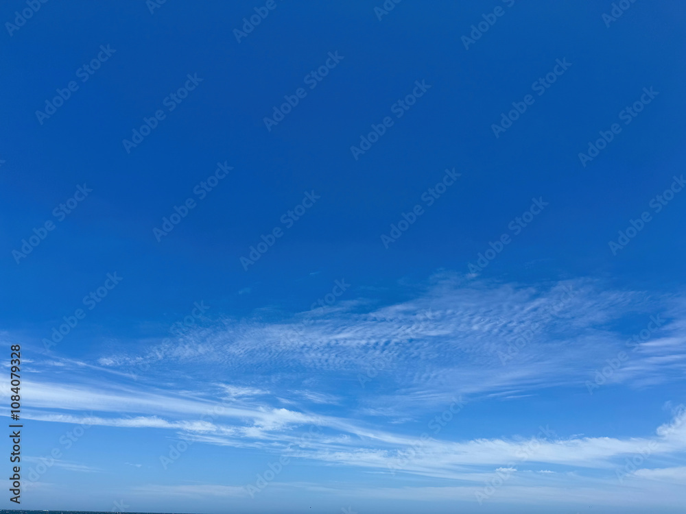 Fototapeta premium Clear blue sky with light, white clouds background. Expansive blue sky and thin scattered clouds