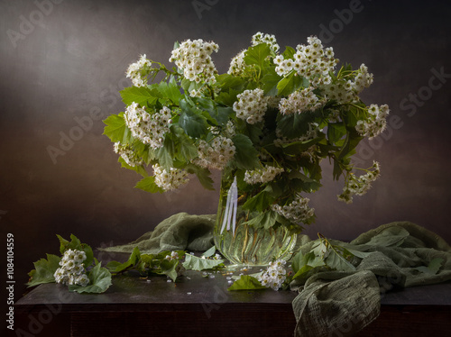 Still life with a bouquet of blooming hawthorn in a glass vase on a dark background photo