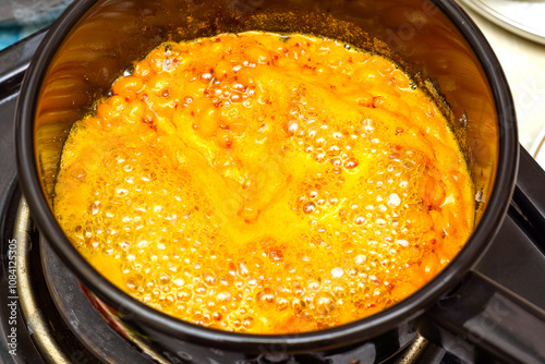 Boiling sea buckthorn berries with granulated sugar in a saucepan for making jam.