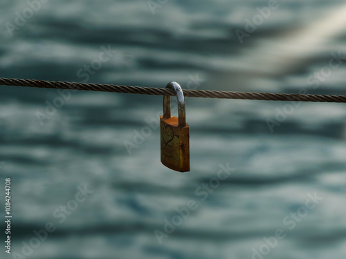 A lock with a heart drawn on its surface hangs from a wire, with a blurred sea in the background, creating a romantic and serene atmosphere. The lock symbolizes eternal love, while the sea 