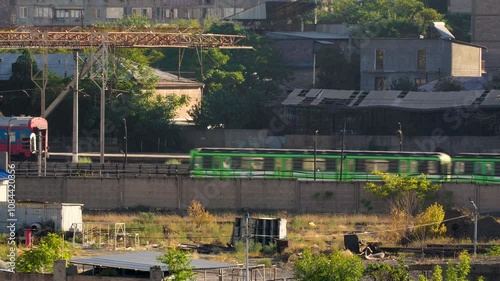 Wallpaper Mural A green and orange train moves through an industrial area with overgrown vegetation and aging structures. Torontodigital.ca