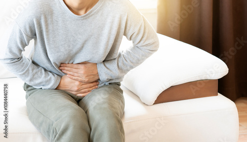 Young woman sitting on a sofa, holding her belly with a painful expression photo