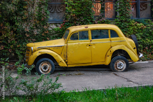 A rare yellow car stands on the street in the open air. Rarity. Near the ivy-covered building there is an old Moskvich-400 with flat tires.