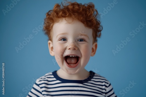 Joyful redheaded child with striped shirt on blue background expressing happiness