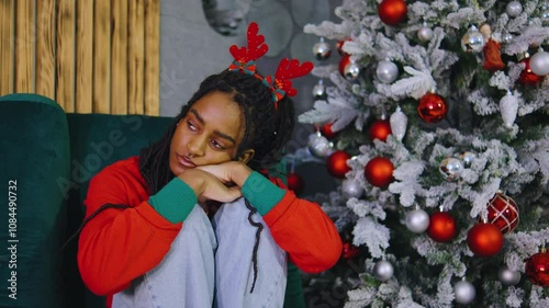 A young woman feels lonely and upset in a Christmas-decorated room. Surrounded by festive decor, she reflects sadly, contrasting with the holiday warmth around her