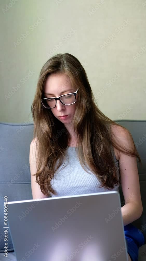 young woman with glasses sits on the sofa and opens a gray laptop. Freelancer girl working from home young woman with glasses sits on the sofa and opens a gray laptop. Freelancer girl working from home