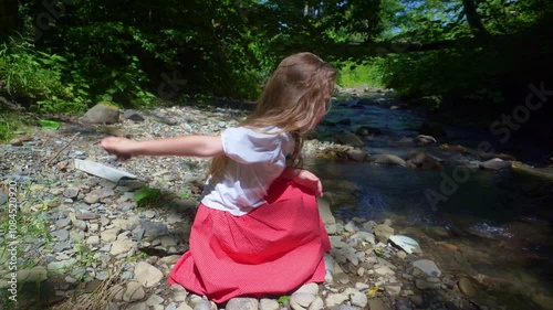 A girl on the bank of a mountain river throws stones into the water.