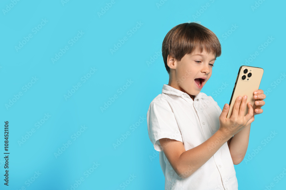 Cute little boy with smartphone on light blue background, space for text Cute little boy with smartphone on light blue background, space for text