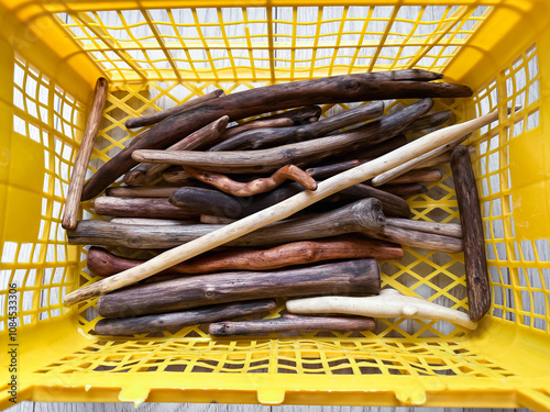 A variety of driftwood sticks in a bright yellow plastic container, showcasing natural textures and earthy hues. Perfect for themes of craftsmanship, resources, organization, or creative materials.