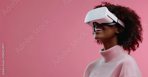 Young woman enjoys virtual reality experience while smiling against a pink ba...
